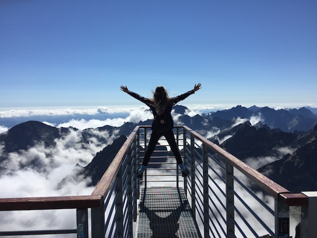 Experiencing the thrill of a new language. A person standing on a railing overlooking a breathtaking mountain range, symbolizing the expansive horizons that language learning can open